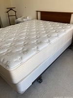 Full view of mattress on foundation and steel frame with wooden headboard visible behind.