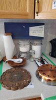 Two large glass containers with metal latch lids on countertop, with ceramic paper towel holder next to them, wood dowel visible inside holder, also ceramic spoon rest in shape of small dish.