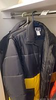 Black and yellow insulated winter coat hanging in closet with partial view of another coat