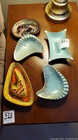 Top view of all 5 MCM ashtrays arranged on wooden surface showing variety in shapes, colors, and repaired metal piece.