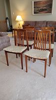 Four wood frame dining chairs grouped together on carpeted floor with slatted backs and upholstered seats visible.
