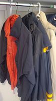 Four men's jackets and coats hanging on a rack showing colors and materials.