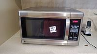 Full view of the GE JES1295 convection microwave oven placed on a kitchen counter with a visible sticker on the door.