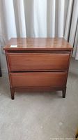 Front view of a two drawer wooden night table with scratches on top surface.
