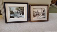 Two framed oil paintings side by side showing winter scenes on carpeted floor