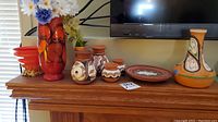 View of multiple Southwestern pottery pieces arranged on a mantel, including small vases, a plate, and a tall vase with flowers.