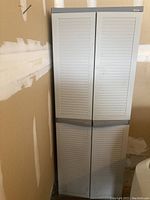 Front view of the closed plastic storage cabinet showing gray louvered double doors with handles.