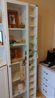 Two white wood cabinets side by side; one with glass door and 5 shelves, another with 12 cubby holes; some decorative items inside glass cabinet.