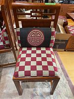 Front angle of wood chair showing red and beige checkered upholstered seat and black back cushion with a red oriental symbol.