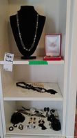 Full view of three shelves showing assorted necklaces, bracelets, and earrings on white shelves
