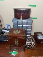 Four distinct jewelry boxes shown together on wooden floor and silver-tone box as pedestal.