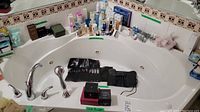 Wide shot of lot displayed around bathroom tub. Includes multiple lotions, powders, fabric softener, and makeup brushes.
