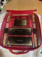 Open makeup kit showing three palettes, lip gloss, lipsticks, and pencils organized inside red case