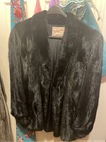 Front view of black women's mink fur jacket on hanger showing collarless design and plush fur.