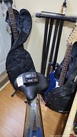 Overview photo showing black keyboard stand, drummer's stool, blue ukulele, electric guitar in soft case, and Dunlop 65 tuner on top of the stand.