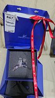 Photo of Swarovski-branded blue box with foam insert holding crystal birds figurine, alongside branded shopping bag and red Swarovski ribbon.