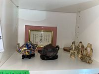 Shelf with the miniature teapots, framed calligraphy, four figurines, and wooden coaster visible
