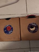 Two 45 RPM vinyl records each in brown paper sleeves; labels include London Records and Capitol Labels with visible song titles and artists.