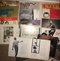 Overview of 15 vinyl albums laid out showing front covers including John Mathis Greatest Hits double album, Edith Piaf, Wilton Felder, Idris Muhammad, Chuck Mangione, and others.
