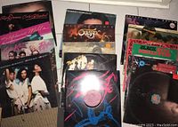 Group shot of 15 vinyl albums showing various artists and colorful album covers, some with price stickers.