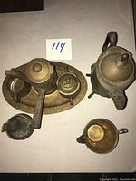 Top down photo of antique metal tea set showing kettle, teapot on tray with a small container, metal tea cup, and smaller open cup.