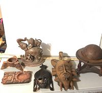 Photo showing six wood carved items including animal figures, masks, a plaque, and a decorative globe.