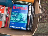 Box with military books including Operation Buffalo, Incursion, US Army Special Forces Medical Handbook, and Secrets of Infantry