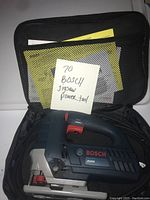 Bosch JS260 jigsaw power tool inside black carrying case with mesh pocket holding the user manual and documentation