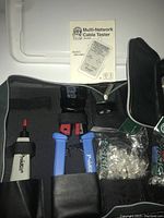 Network cable tester kit layout showing tools including punch down tool, wire stripper, manual, and probe pen arranged in black case