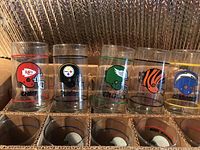 Front row of NFL drinking glasses showing Kansas City Chiefs, Pittsburgh Steelers, Philadelphia Eagles, Cincinnati Bengals, and Los Angeles Chargers helmets and logos.