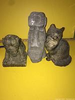 Front view of the three stone door stops on yellow background showing pug dog, owl, and cat figures with worn surfaces.