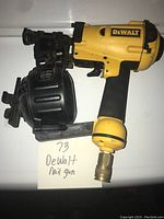 Side view of yellow and black DeWalt nail gun with attached drum magazine and air fitting.