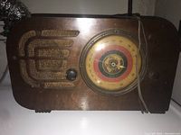 Front view of the vintage wooden radio showing the circular dial with frequency markings and tuning knob on the right, and the art deco styled speaker grille on the left.