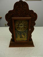 Antique gingerbread wooden mantel clock with ornately carved scrollwork surrounding the glass door showing a heron design.