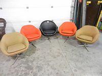 Five mid-century modern swivel chairs in an industrial setting, colors tan, orange, and black, showing overall wear and faded upholstery.