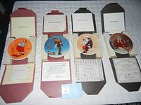 Four Norman Rockwell Christmas collector plates displayed in original boxes with respective certificates of authenticity laid out beneath each plate.