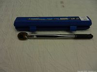 Torque wrench laid flat with blue plastic carrying case behind it