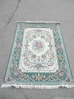 Full view of the rectangular area rug showing the ivory central section with floral motifs and the forest green patterned border with fringe edges.