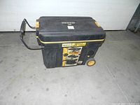 Front angled view of the black and orange mobile tool chest showing wheels, handle, and label.