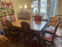 Photo showing a set of 8 antique dining chairs arranged around a wooden table in a room with large windows and paintings.