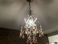 Front angled view of the ornate antique hall chandelier showing glass droplets and crystal beads suspended from metal arms.