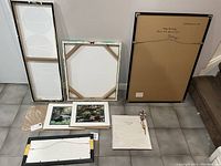 Overview of back sides of several framed art pieces showing canvas, backing, and signature