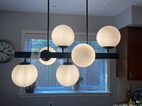 Side view of the ceiling light fixture showing six frosted globe lights on a horizontal black metal frame with two suspension rods.
