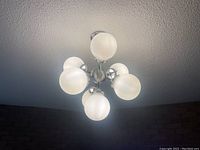 Chandelier ceiling light fixture with six frosted glass globes illuminated, showing metal frame and globes.