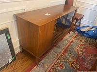 Angled front view of buffet showing wood door on left, sliding glass doors center, tapered legs.