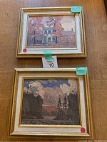 Two framed art reproductions, one depicting houses in autumn, the other a dark forested landscape under cloudy sky.
