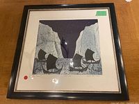Front view of framed lithograph artwork showing stylized ships, cliffs, and night sky, with visible signature and red dot sticker on mat.