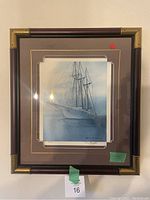 Framed lithograph showing a three-masted sailing ship in blue tones with a wooden frame and gold corner accents.