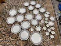 Photo showing full china set laid out on carpet including dinner plates, soup bowls, serving platter, and additional small dishes.