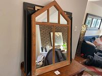 Front view of the antique wooden frame mirror leaning on a surface with other frames behind it, showing the reflective glass divided into panes.